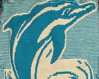 May include: A crocheted blanket featuring a blue dolphin jumping out of the water. The dolphin is white with blue accents and is surrounded by white waves.