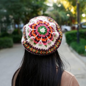 May include: A white knitted beanie with a colorful floral pattern in shades of orange, pink, green, and brown.