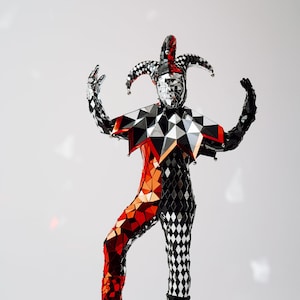 Pode incluir: Um traje de bufão com um padrão de losangos vermelho e preto, um acabamento espelhado e um chapéu pontudo com sinos. O traje é feito de um material brilhante e reflexivo.