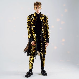 May include: A person wearing a black long-sleeved jacket with gold sequins and black pants with gold sequins. The person is standing on a white background.