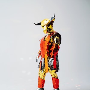Puede incluir: Una persona que lleva un traje de espejo rojo y dorado con cabeza de toro. El traje está hecho de muchas piezas pequeñas y reflectantes.
