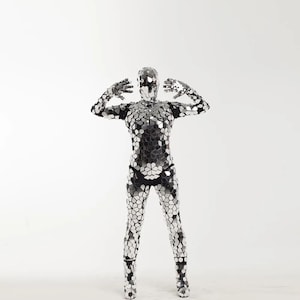 May include: A person wearing a silver mirrored bodysuit with a geometric pattern. The bodysuit covers the entire body, including the head, arms, and legs.