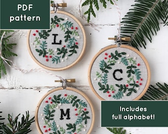May include: Three embroidered Christmas ornaments with a wreath design and a letter in the center. The letters are L, C, and M. The ornaments are on a white wooden background. Includes full alphabet! PDF pattern.
