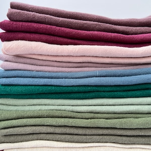 May include: A stack of folded linen fabric in various colors, including burgundy, pink, blue, green, and beige.