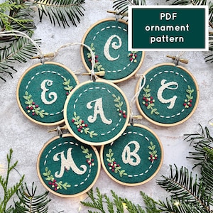 May include: Six green felt ornaments with white letters embroidered on them. The letters spell out the word "MERRY". Each ornament has a small red berry design around the letter. The ornaments are arranged in a circle on a white surface. PDF ornament pattern.