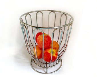 May include: A silver wire fruit basket with a round base and four red apples inside.
