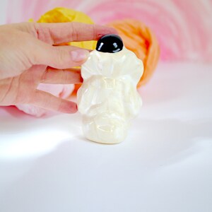May include: A white ceramic figurine of a person wearing a hat with a black top. The figurine is standing on a white surface.