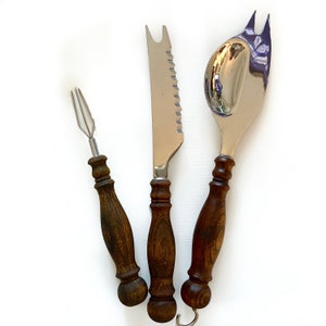 Op de afbeelding: Een set van drie keukengerei met houten handvatten. De keukengerei omvatten een kaasmes, een serveersvork en een kleine vork.