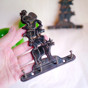 May include: A black metal key holder with a rooster, a duck, and a cow design. The key holder has three hooks.