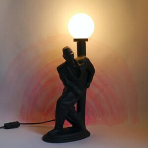 May include: A black lamp shaped like a man holding a lamppost with a white globe light on top.