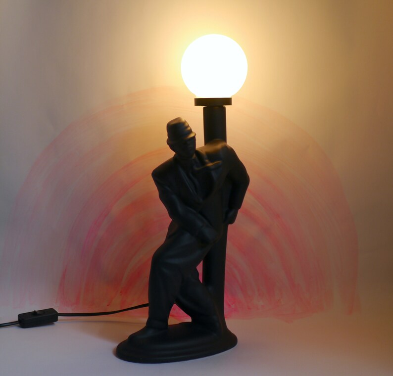 May include: A black lamp shaped like a man holding a lamppost with a white globe light on top.