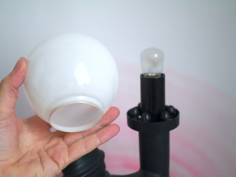 May include: A white glass lampshade with a black lamp base. The lamp base has a round, black ring with small, black balls around the edge.