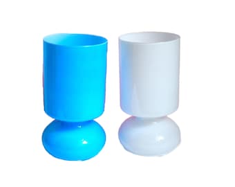 May include: Two plastic candle holders, one blue and one white. Both have a cylindrical top and a rounded base.