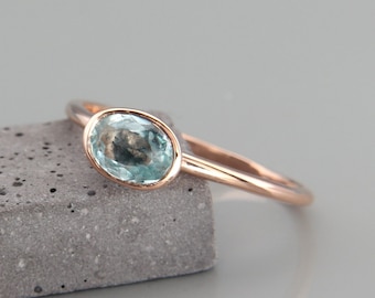 May include: A delicate rose gold ring with a light blue oval gemstone.