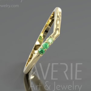 Puede incluir: Un anillo de banda de oro con un diseño de chevron engastado con cuatro pequeñas piedras preciosas verdes.