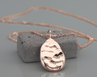 May include: A rose gold necklace with a hammered, teardrop-shaped pendant.