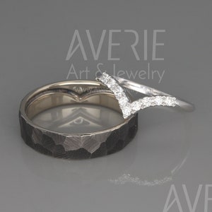 May include: A pair of wedding bands. The main band is a hammered black metal band. The second band is a thin white metal band with a V-shaped row of small diamonds.