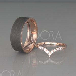 May include: A pair of wedding bands. One band is a wide, black, matte finish band. The other band is a thin, rose gold band with a V-shaped row of small diamonds.