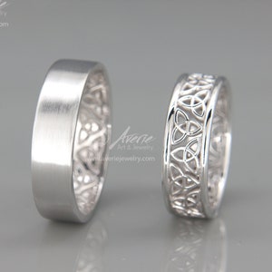 Könnte beinhalten: Zwei silberne Eheringe. Ein Ring ist glatt und der andere hat ein keltisches Knotendesign.