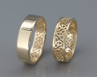 Könnte beinhalten: Zwei goldene Eheringe. Ein Ring ist glatt und der andere hat ein keltisches Knotendesign.