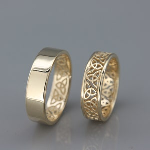 Könnte beinhalten: Zwei goldene Eheringe. Ein Ring ist glatt und der andere hat ein keltisches Knotendesign.