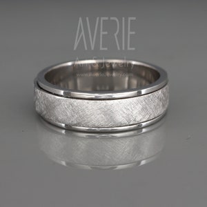 May include: A silver spinning wedding band with a brushed finish. The band has a groove around the edge.