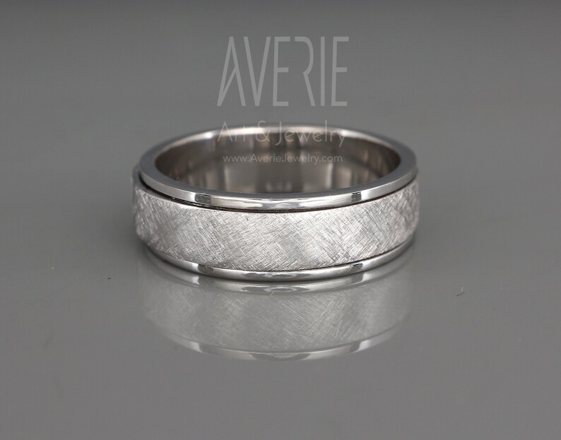 May include: A silver spinning wedding band with a brushed finish. The band has a groove around the edge.