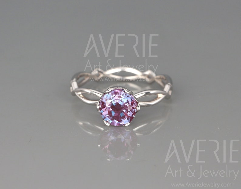 Op de afbeelding: Een zilveren ring met een gedraaide band en een ronde, gefacetteerde, paarse en blauwe edelsteen.