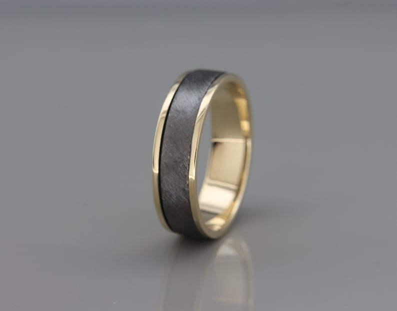 May include: A black and gold wedding band with a brushed finish. The band has a thin gold edge.