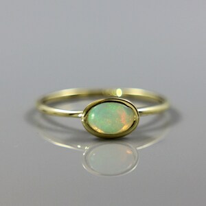 May include: A delicate gold ring with a light green oval opal gemstone.