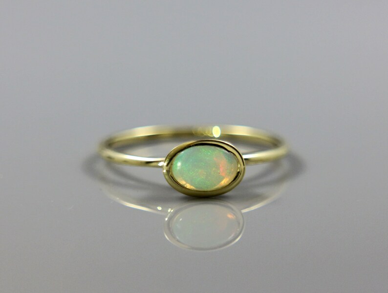 May include: A delicate gold ring with a light green oval opal gemstone.