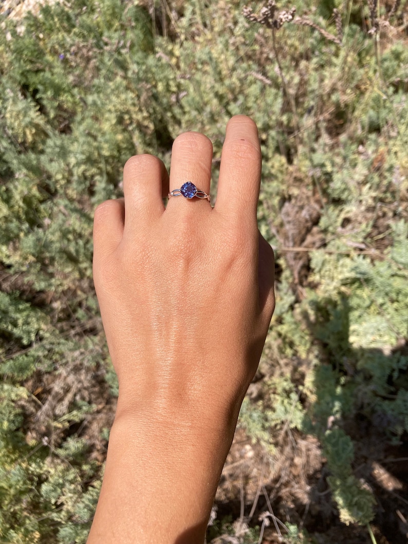 Op de afbeelding: Een delicate ring met een paarse edelsteen gezet in een zilveren band. De ring wordt gedragen aan een vinger.