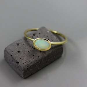 May include: A gold ring with a white opal gemstone set in a bezel setting.