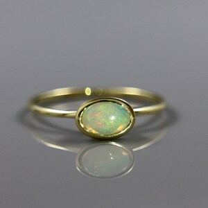 May include: A delicate gold ring with a pale green opal gemstone set in a bezel setting.