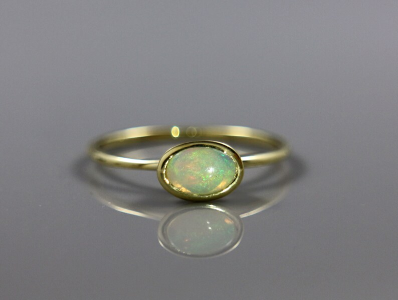 May include: A delicate gold ring with a pale green opal gemstone set in a bezel setting.