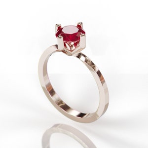May include: A gold ring with a red ruby gemstone set in a prong setting.