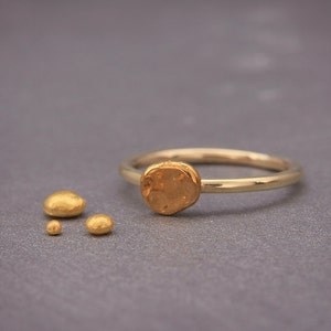 May include: A gold ring with a textured, round, gold accent. The ring is on a grey surface with three smaller, textured, gold pieces.