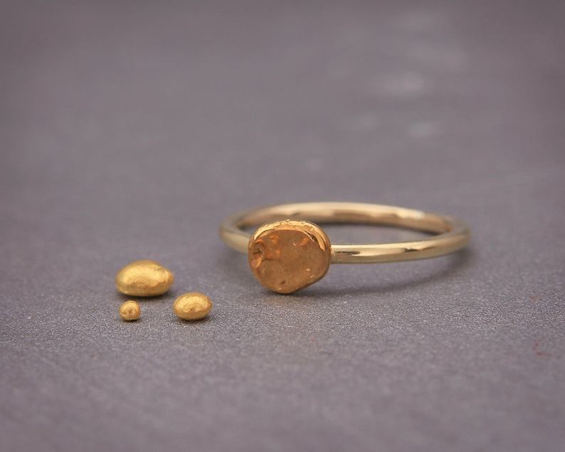 May include: A gold ring with a textured, round, gold accent. The ring is on a grey surface with three smaller, textured, gold pieces.
