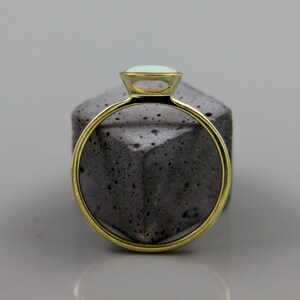 May include: A gold ring with a light blue opal gemstone set in a bezel setting.
