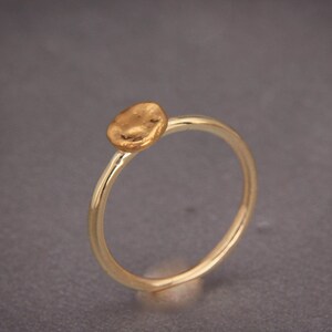 May include: A simple gold ring with a textured, round, flat top.