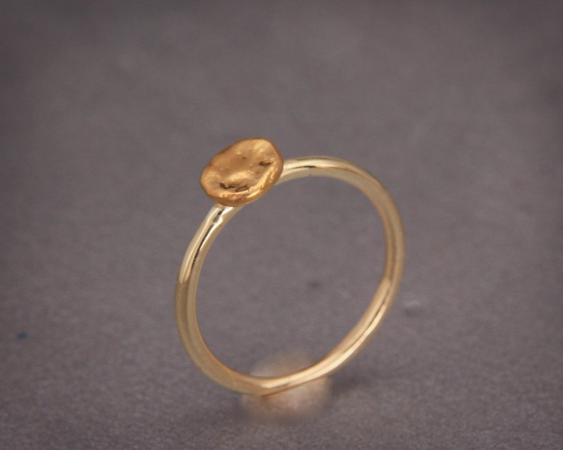 May include: A simple gold ring with a textured, round, flat top.