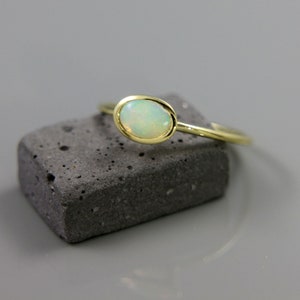 May include: A delicate gold ring with a white opal gemstone. The ring is set on a gray stone surface.