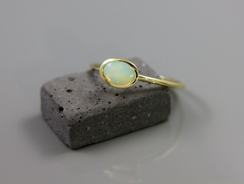 May include: A delicate gold ring with a white opal gemstone. The ring is set on a gray stone surface.
