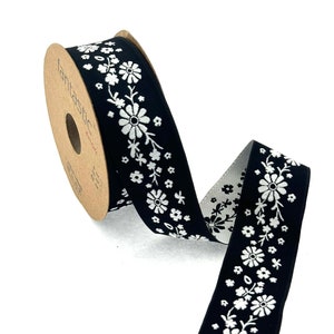 以下が含まれることがあります： 白い花の模様が入った黒いリボン。リボンは、「Fantastic」と印刷されたリールに巻かれています。