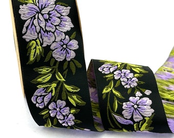 Puede incluir: Cinta negra con un patrón floral en tonos de morado y verde. Las flores están bordadas en la cinta.