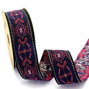 May include: A spool of decorative ribbon featuring a repeating pattern of dark purple and vibrant pink geometric shapes with silver metallic accents. The edges of the ribbon are finished with a thin black border containing small white square details.