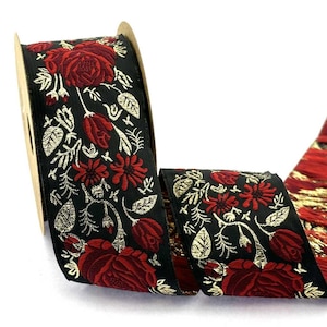 Könnte beinhalten: Eine Rolle schwarzes Band mit einem gewebten Muster aus dunkelroten Rosen und metallisch goldenen Blättern. Das florale Design wiederholt sich über die gesamte Länge des Stoffes und zeigt eine komplexe Stickerei mit dunkelroten Blütenblättern.