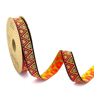 Może przedstawiać: Szpula pomarańczowej, różowej, zielonej i czarnej wstążki z geometrycznym wzorem. Wstążka znajduje się na brązowej szpuli z nadrukowanym słowem "Fantastic".