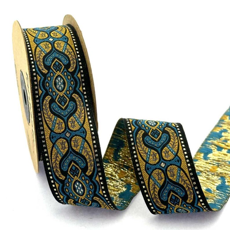 May include: A spool of woven ribbon featuring a repeating pattern in teal, gold, and black. The design includes intricate symmetrical shapes with a metallic gold sheen and a black border with small white dots, wound around a cardboard core.
