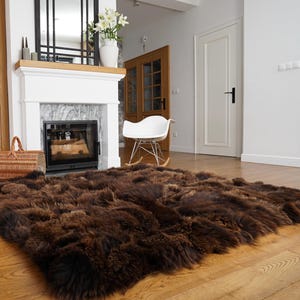May include: A brown sheepskin rug with long, soft fur. The rug is laid out on a hardwood floor in a living room setting.